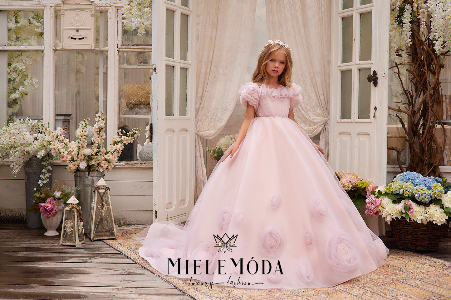 pretty flower girl wearing pink tulle dress with 3d flowers standing in front of open doors at a wedding