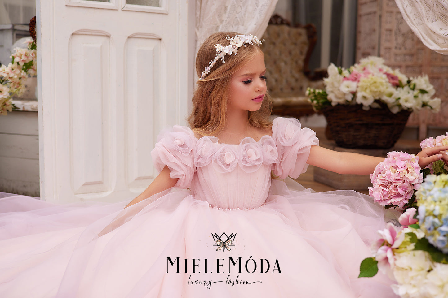 beautiful blond flower girl wearing flower crown and pink chiffon floral gown holding flowers
