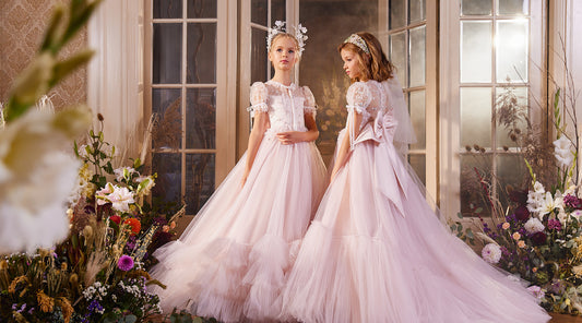 two gorgeous girls wearing pink luxury flower girl gowns by miele moda posing among flowers with headpieces