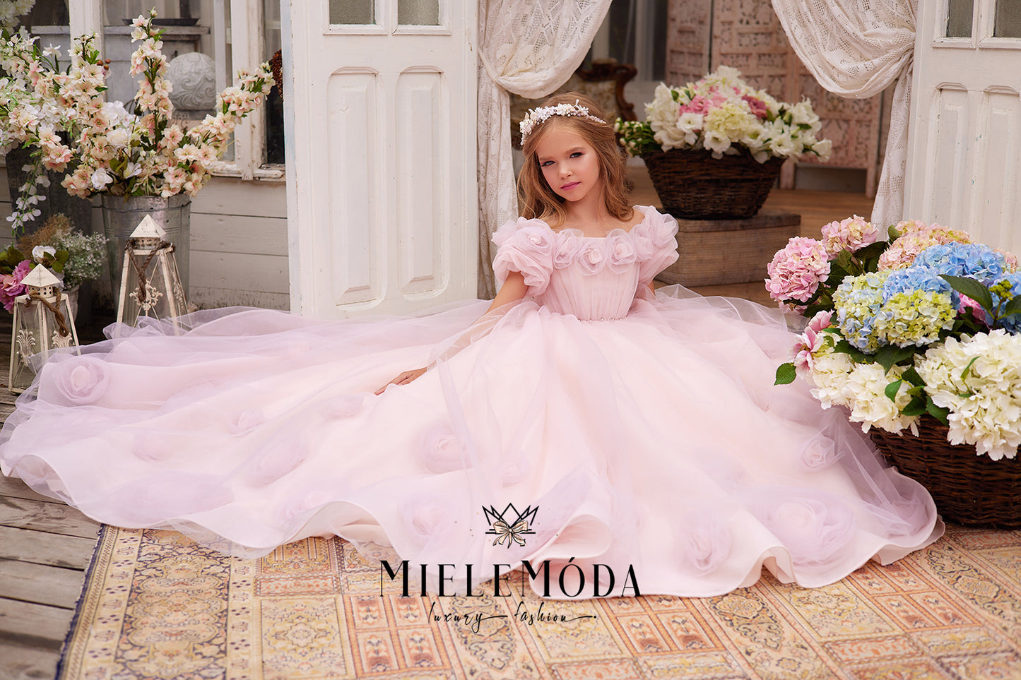 pretty flower girl wearing pink tulle dress with 3d flowers sitting surrounded by beautiful flower baskets