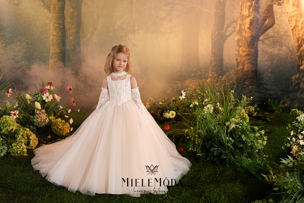 A young girl stands in a fantasy forest setting wearing a formal off-the-shoulder ball gown. The dress has a white lace bodice and a voluminous tulle skirt in a soft blush or champagne tone.