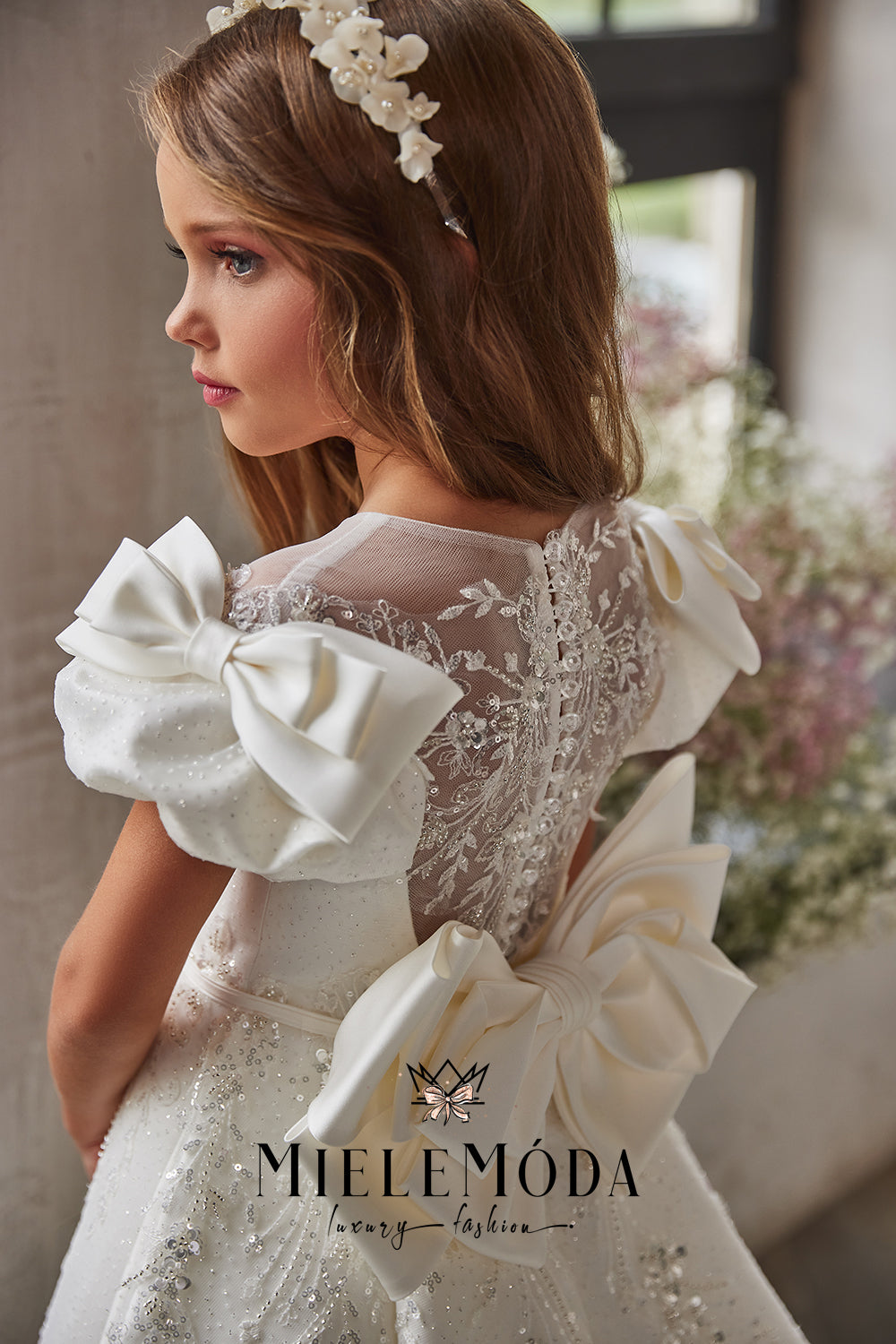 girl looking out the window in her first communion ivory lace dress with bows