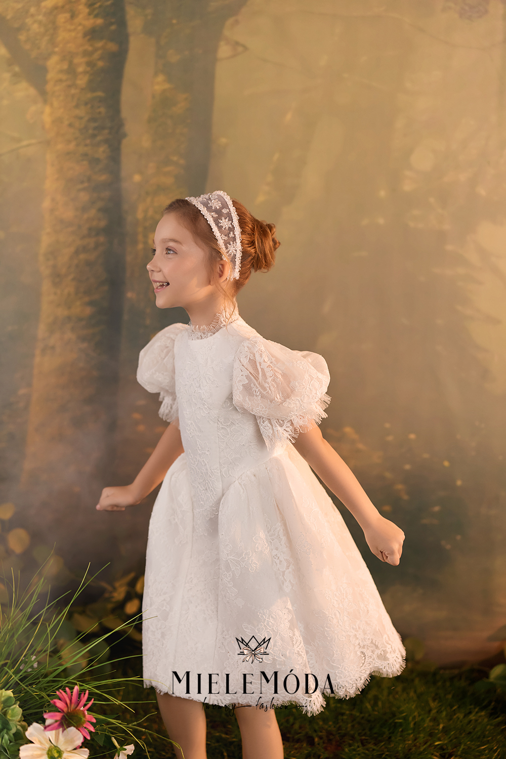 A young girl with red hair in a bun wearing a white lace dress with puff sleeves and a matching lace headband, standing in a misty, golden-toned forest setting.
