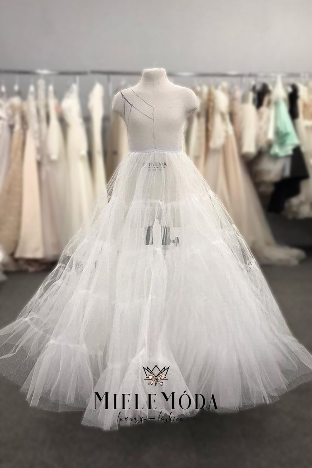 White pettiskirt for special occasion gown on a mannequin with 'Miele Moda' branding in a clothing store setting.